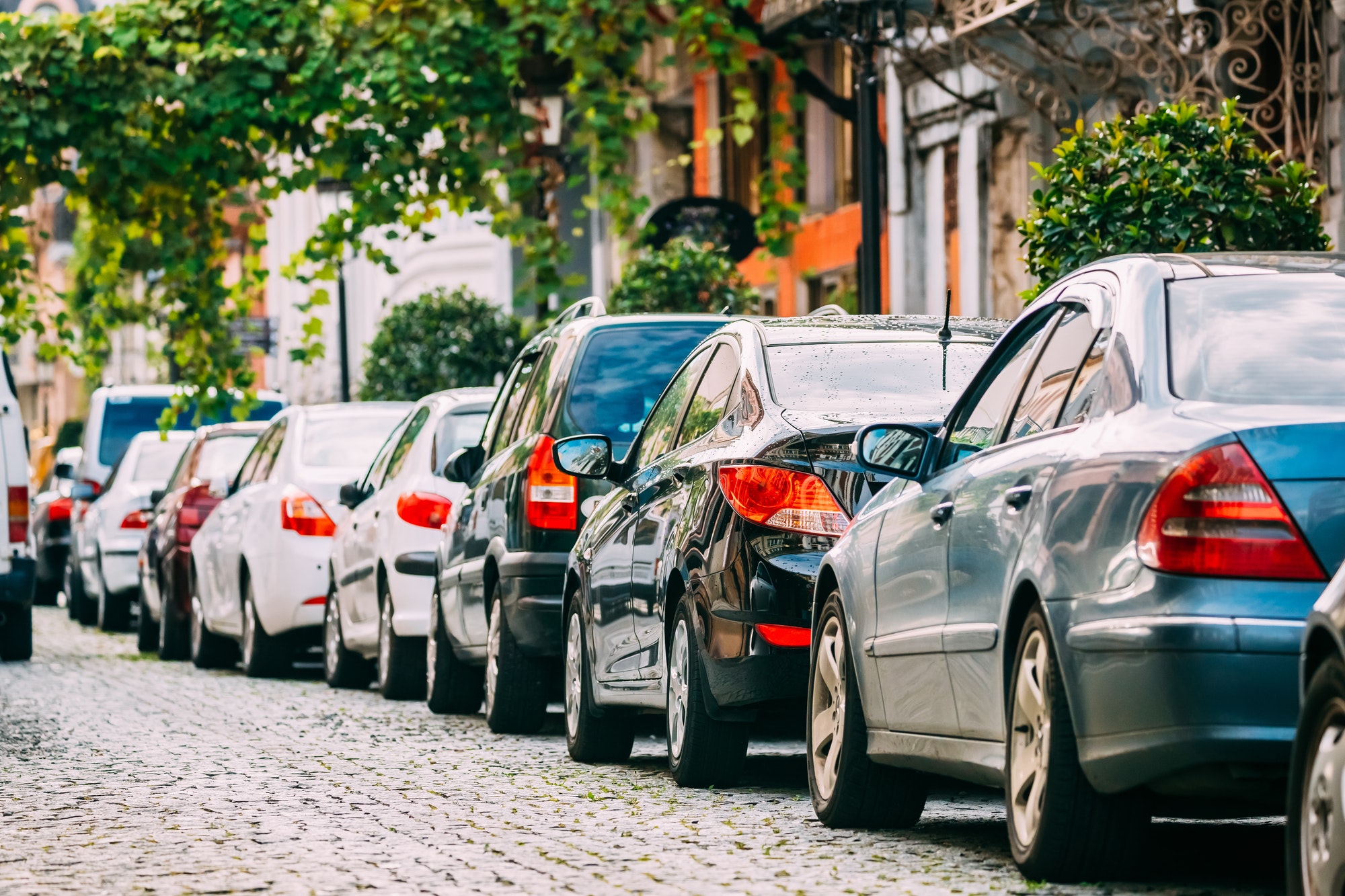 Many Cars Parked On Street In City In Sunny Summer Day. Row Of C